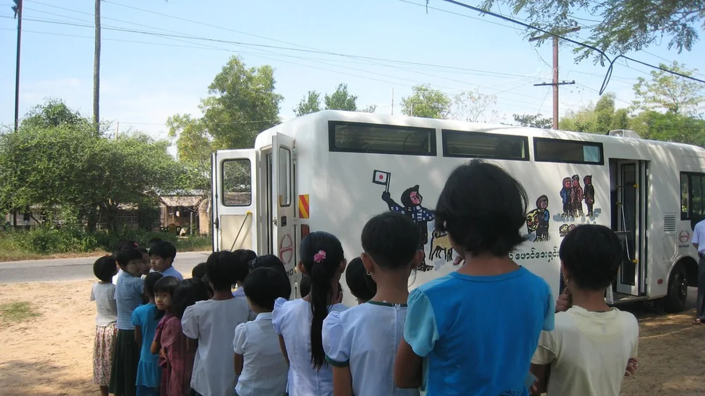 Bibliobús abierto atiende a lectores en una pequeña plaza rural.