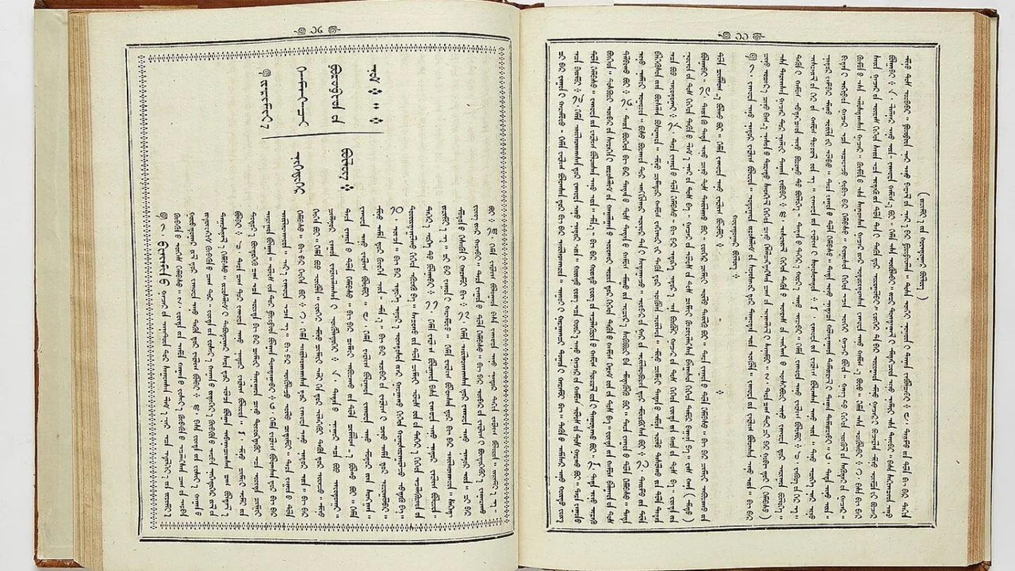 Una tableta muestra columnas verticales de escritura mongola junto a un libro impreso.