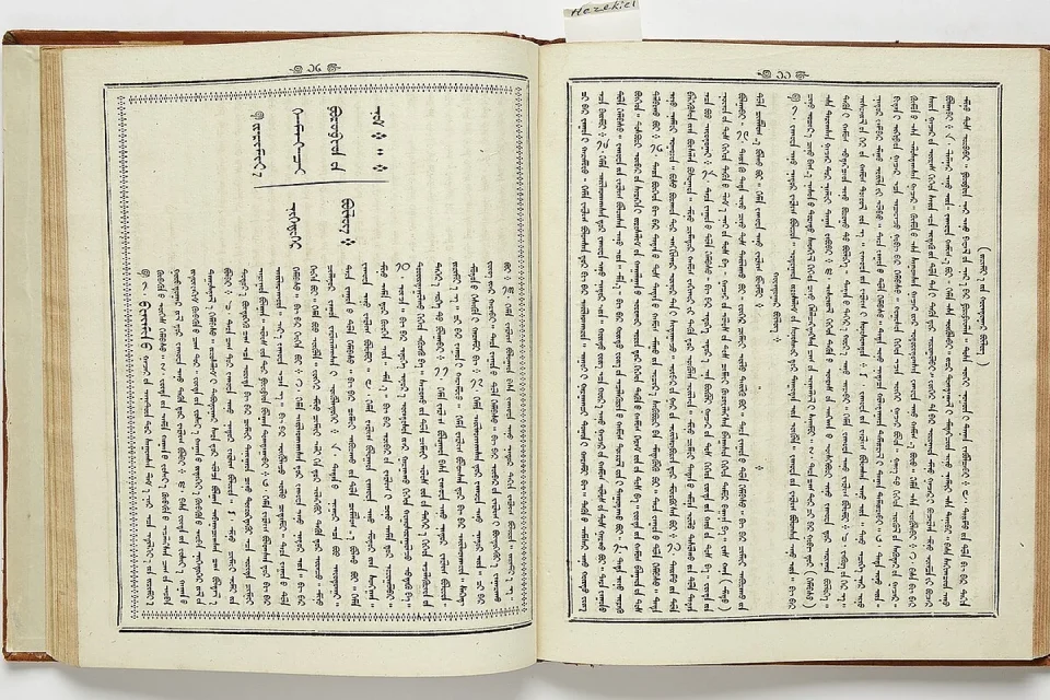 Una tableta muestra columnas verticales de escritura mongola junto a un libro impreso.